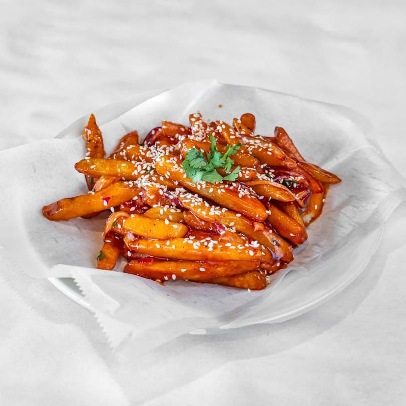 Indian-style chili garlic fries, coated in a glossy red sauce, topped with sesame seeds and cilantro.