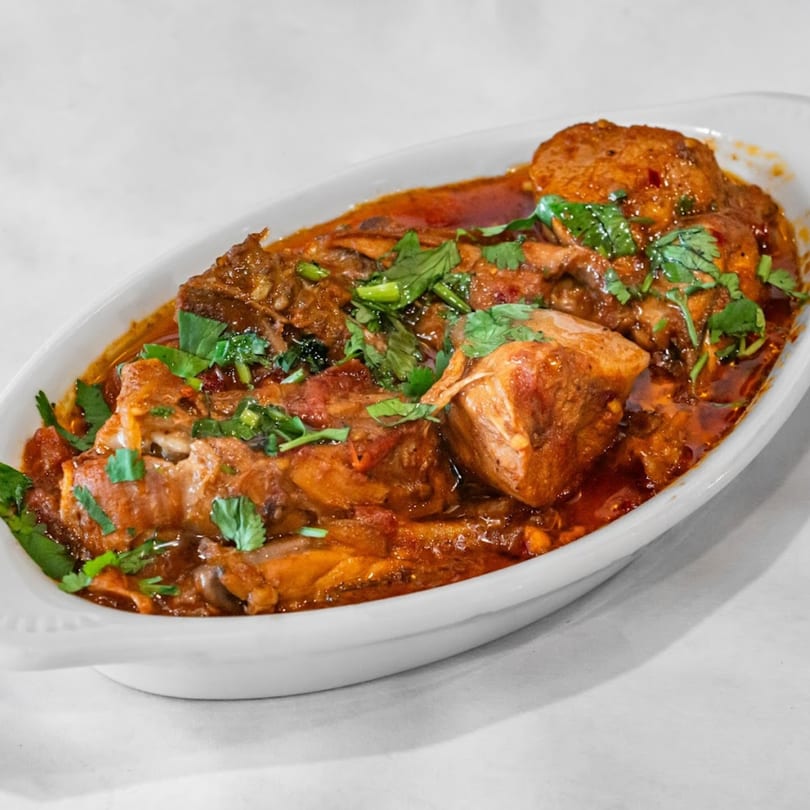 Aladdin Indian & Pakistani Restaurant's chicken curry, garnished with fresh cilantro, in a white oval dish.