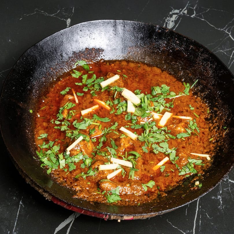 A karahi dish with chicken in a rich, spicy sauce, garnished with fresh cilantro and ginger.