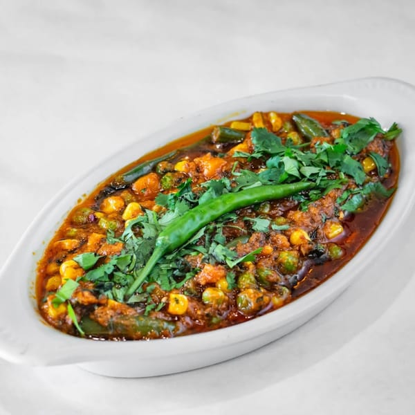 A white oval dish filled with a vibrant Indian vegetable curry, garnished with fresh cilantro and a green chili.