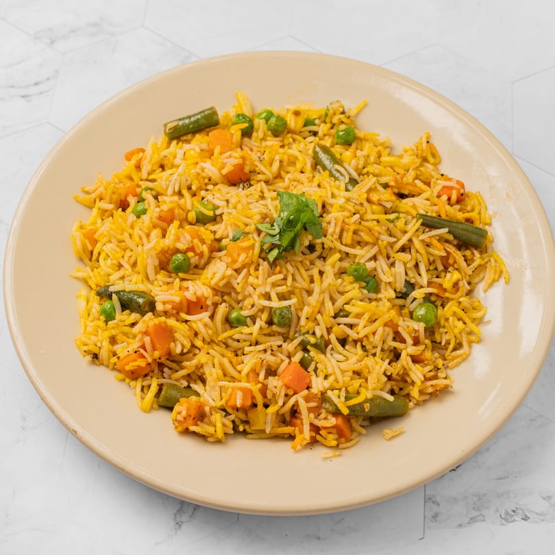 A plate of Indian vegetable biryani with rice, peas, carrots, and green beans, garnished with cilantro.