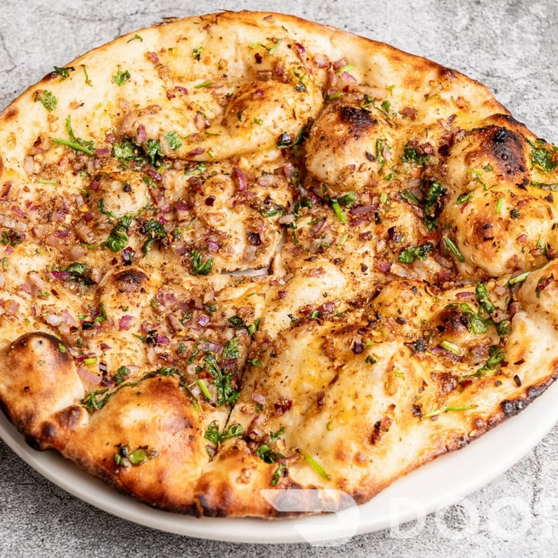 Close-up of a golden-brown Indian naan bread topped with red onions and fresh cilantro.