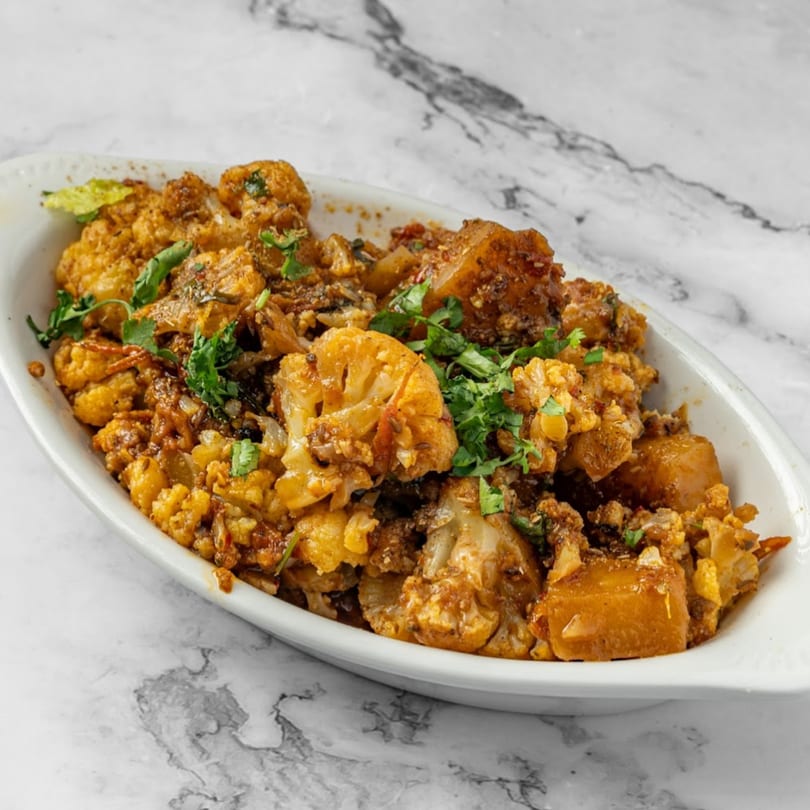 Indian Aloo Gobi, a spiced cauliflower and potato dish, garnished with fresh cilantro in a white serving dish.