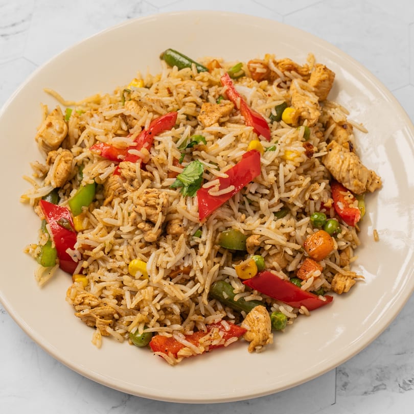 A close-up of chicken fried rice with red bell peppers, corn, peas, and carrots on a white plate.