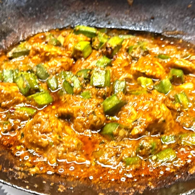 Close-up of a vibrant Indian curry with okra and chicken in a rich, orange sauce.