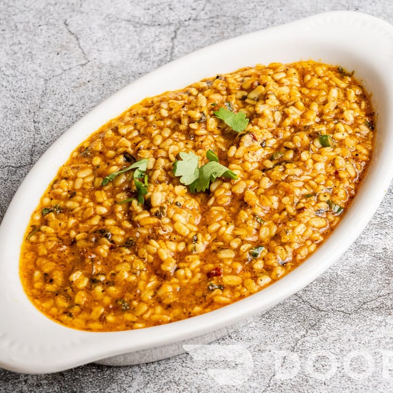 A white oval dish filled with Indian dal, garnished with fresh cilantro, on a gray textured surface.