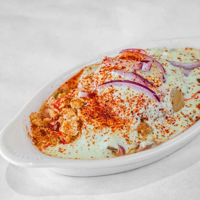 Indian Dahi Bhalla Chaat, topped with yogurt, red onions, and chili powder in a white dish.