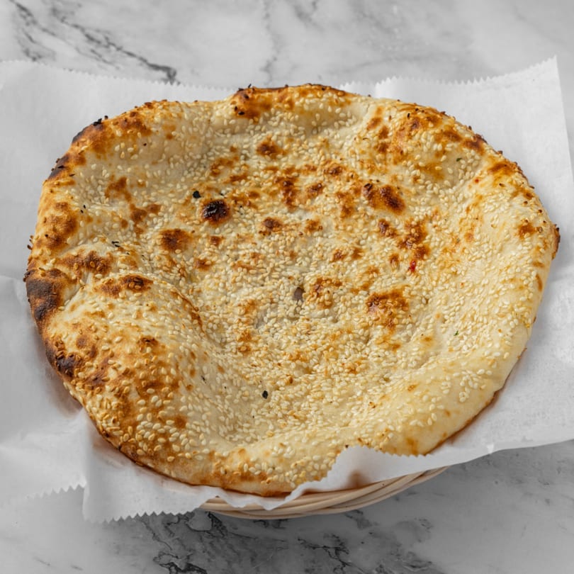 Freshly baked Indian naan bread, topped with sesame seeds, served in a basket.
