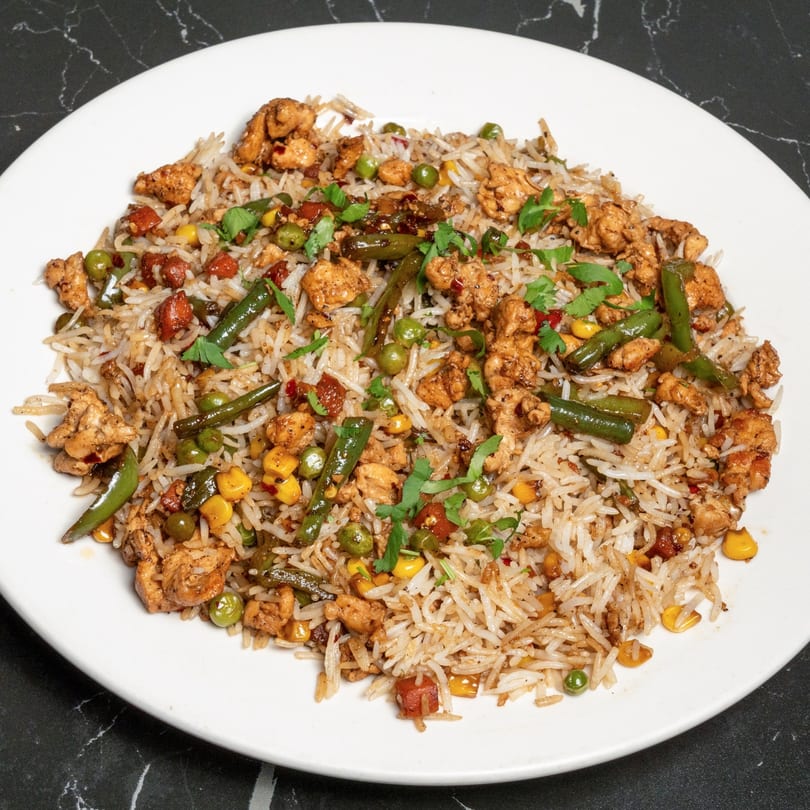 Chicken fried rice with green beans, peas, corn, and red peppers, garnished with cilantro.