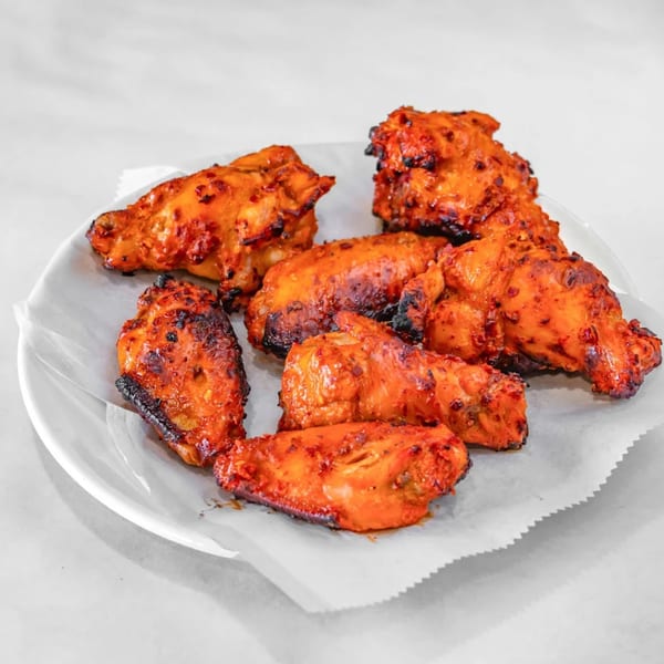 A white plate holds several pieces of Aladdin Indian & Pakistani Restaurant's spicy grilled chicken wings.