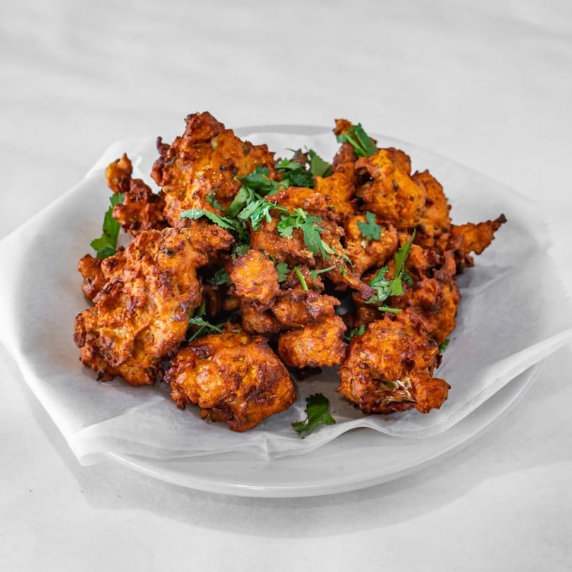 A plate of golden-brown Indian pakoras, garnished with fresh green cilantro, on a white plate.