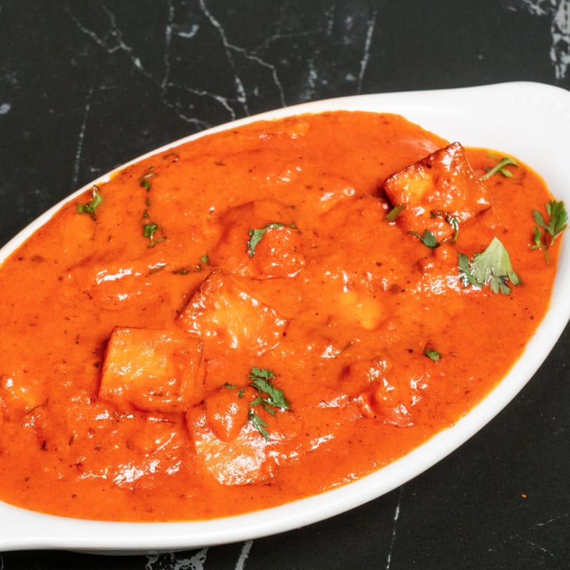 Paneer butter masala, a vibrant orange curry with paneer cubes and cilantro, in a white dish.