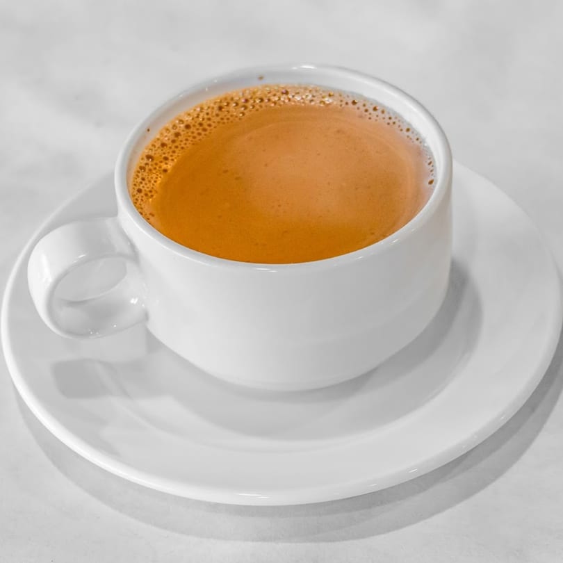 A white cup of Indian chai tea with a frothy top, served on a white saucer.