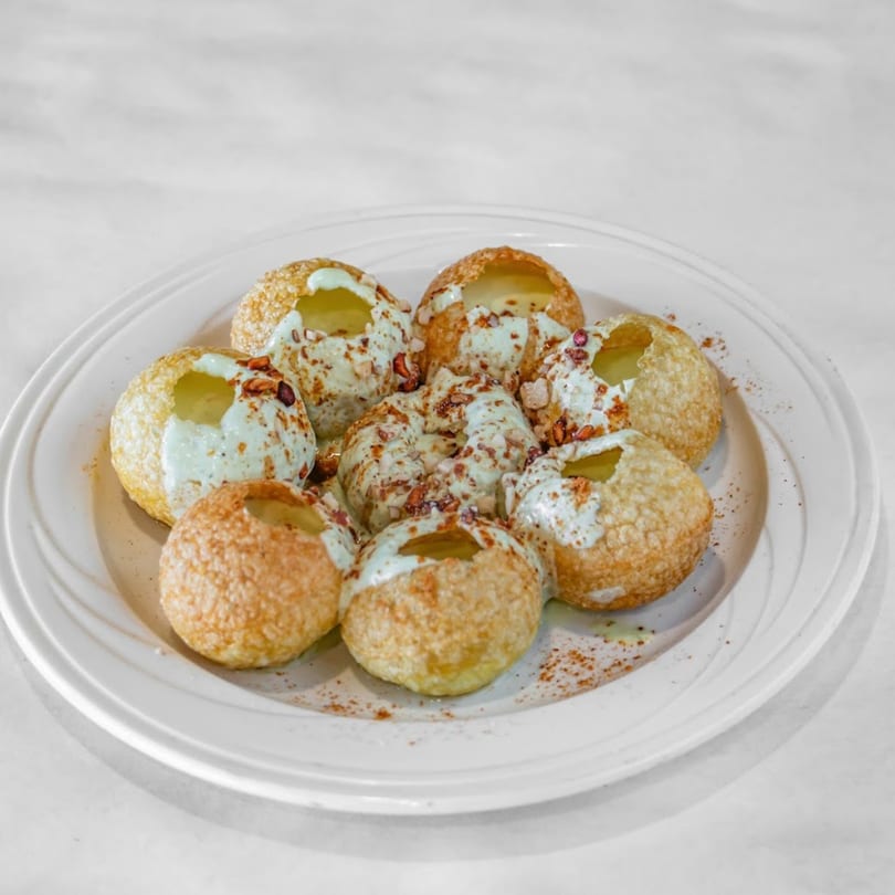 A plate of Indian pani puri, golden-brown and filled with a creamy sauce and nuts.