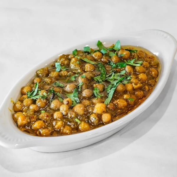 A white oval dish filled with Indian chana masala, garnished with fresh green cilantro.